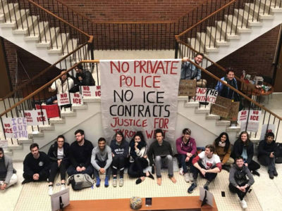 Members of Johns Hopkins Students Against Private Police and Hopkins Anti-ICE Coalition sit under a banner on April 4, 2019, in the university president's office building after sitting in overnight.