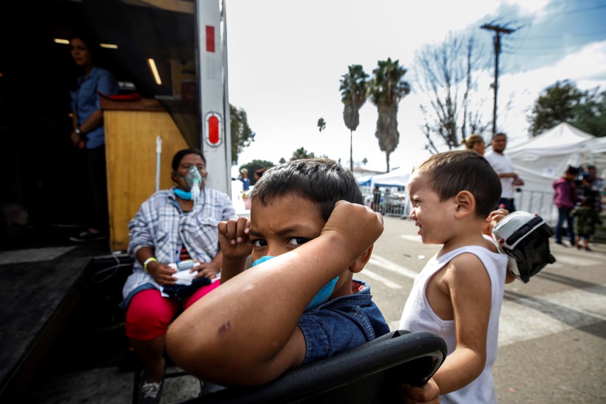 A young boy wearing a face mask stares at the camera while he waits for medical care