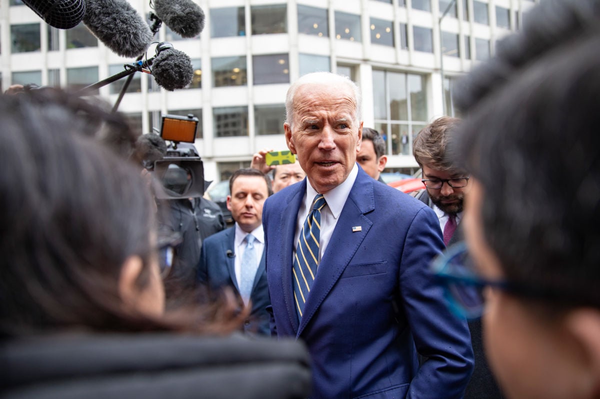 Joe Biden stands amidst journalists on a sidewalk