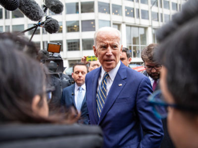 Joe Biden stands amidst journalists on a sidewalk