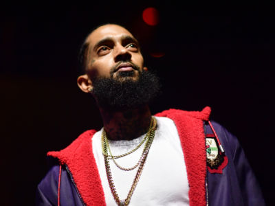 Nipsey Hustle stands in a darkened environment