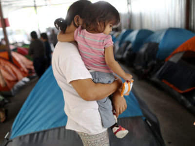 A woman holds her young daughter while standing among tents