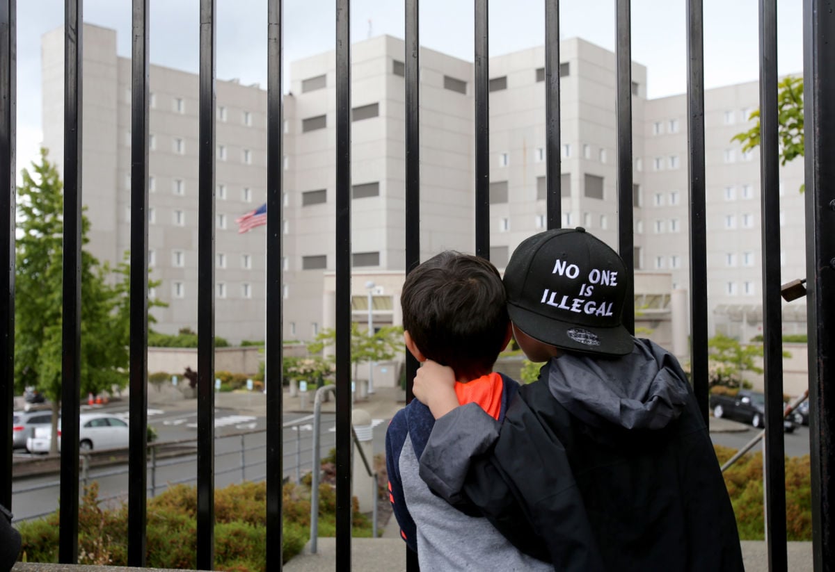 Two children look through a chail link fence at a detention center