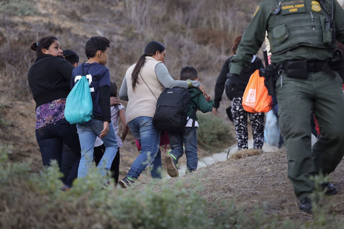 Members of the migrant caravan walk past a U.S. Border Patrol agent at the U.S.-Mexico border fence on December 2, 2018, in Tijuana, Mexico.