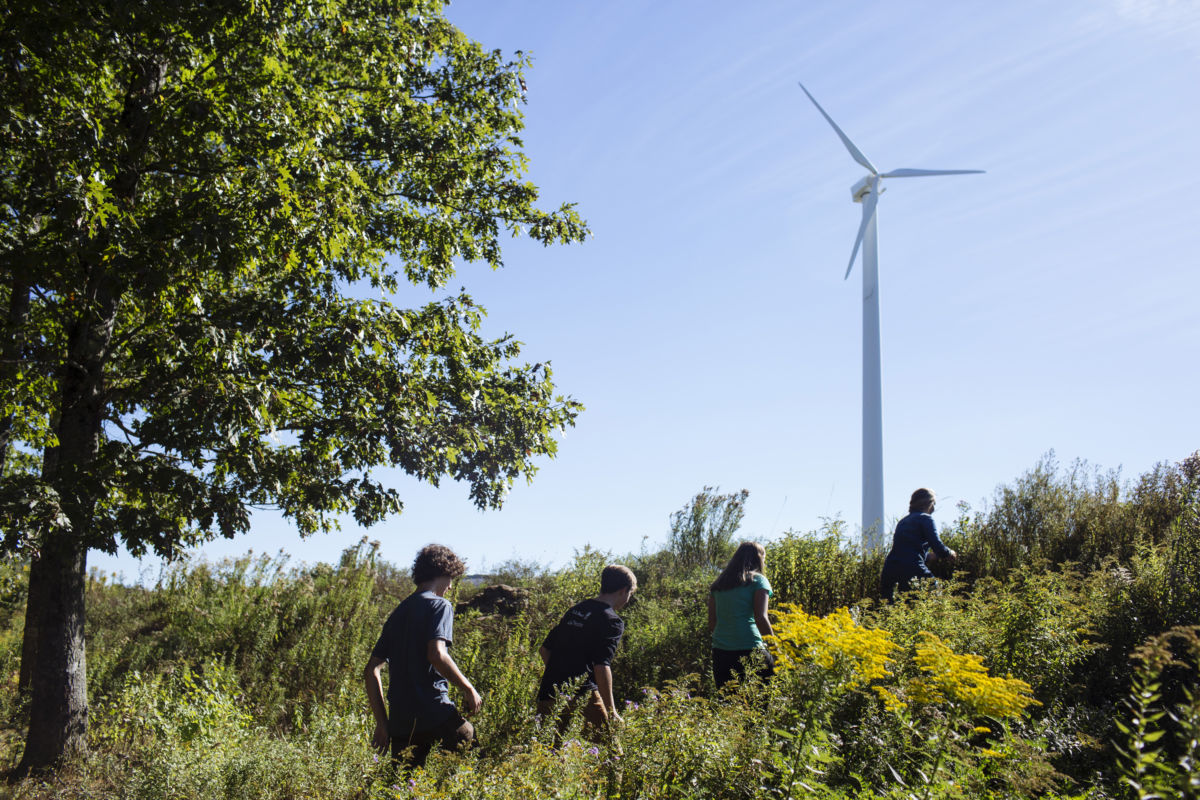 Four children walk up a hill toward a wind turbine