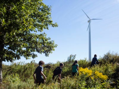 Four children walk up a hill toward a wind turbine