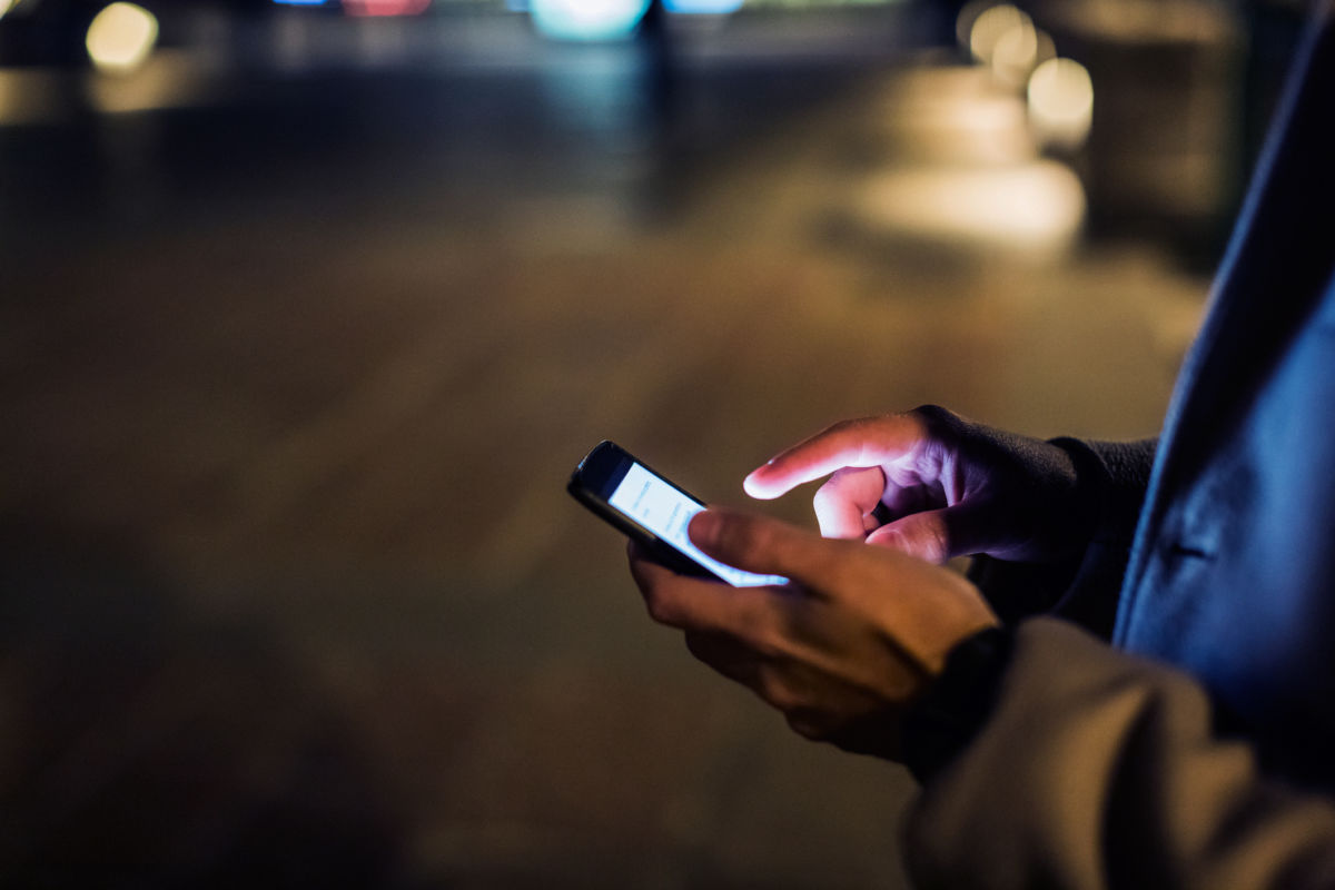 A man holds a cellphone on a darkened street