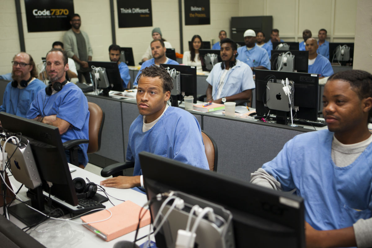 Prisoners in blue sit at a desk with computers during a lecture