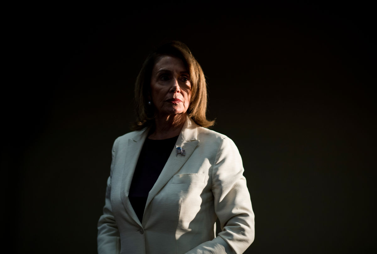 Nanci Pelosi stands in a darkened room