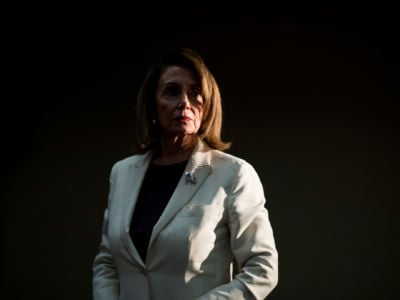 Nanci Pelosi stands in a darkened room