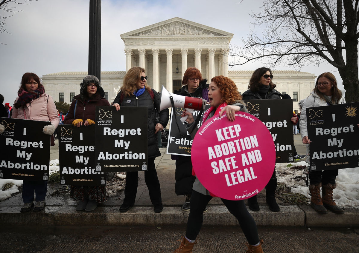 A woman carrying a pro-choice sign speaks into a bullhorn while walking in front of pro-lifers