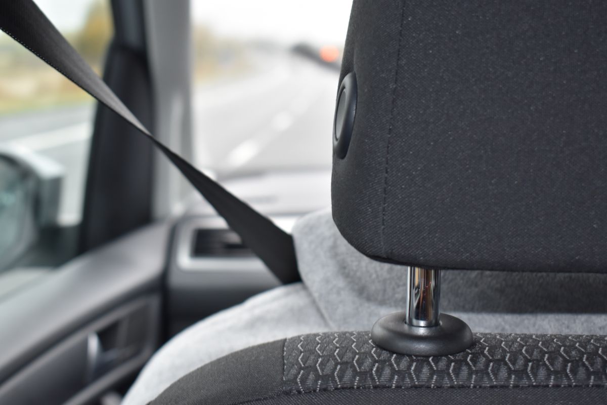 A stock photo of a person sitting in a car from behind. The seatbelt is stretched across them.