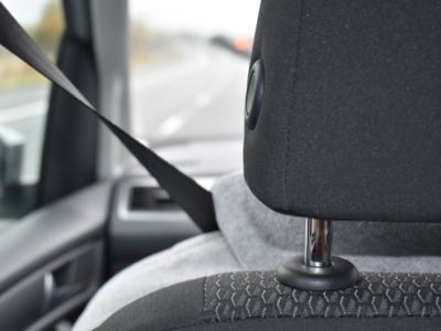 A stock photo of a person sitting in a car from behind. The seatbelt is stretched across them.