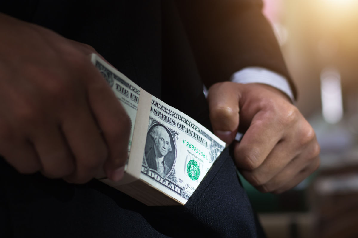 A man puts a stack of dollar bills into his suit pocket