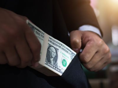 A man puts a stack of dollar bills into his suit pocket