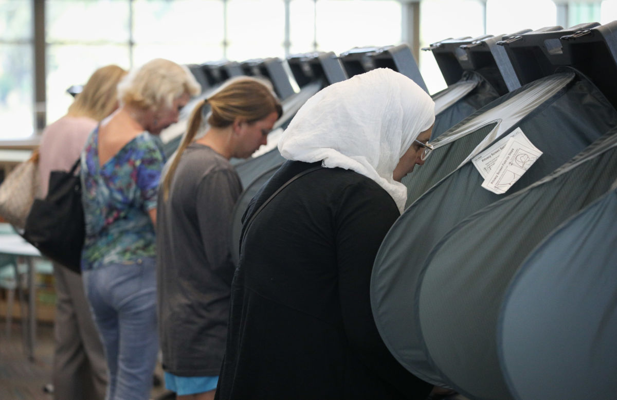 A hijabi stands at a black voting booth