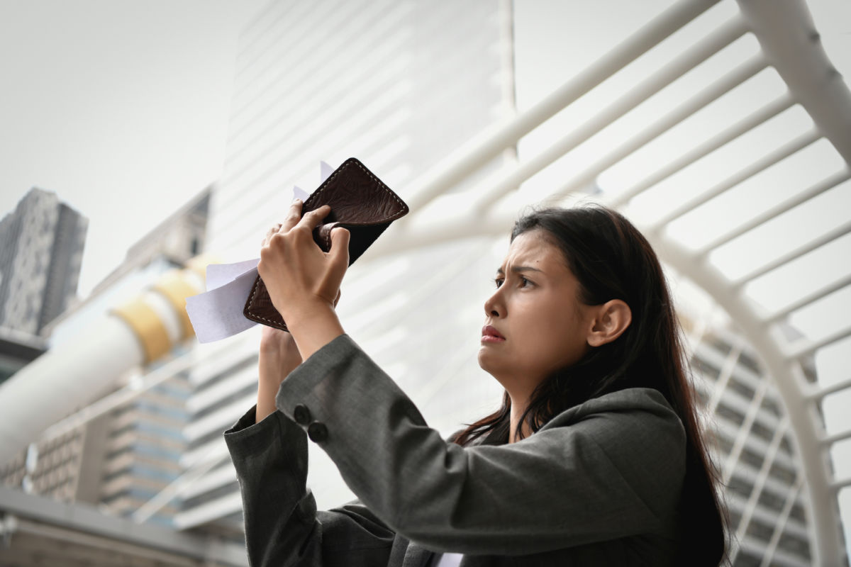 A woman looks mournfully into her empty wallet
