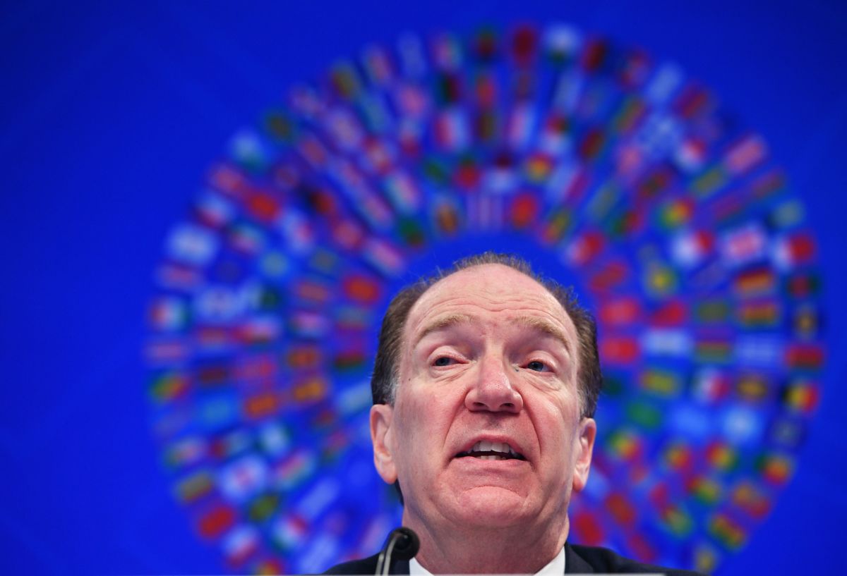 David Malpass sits in front of a sign displaying world flags in a halo