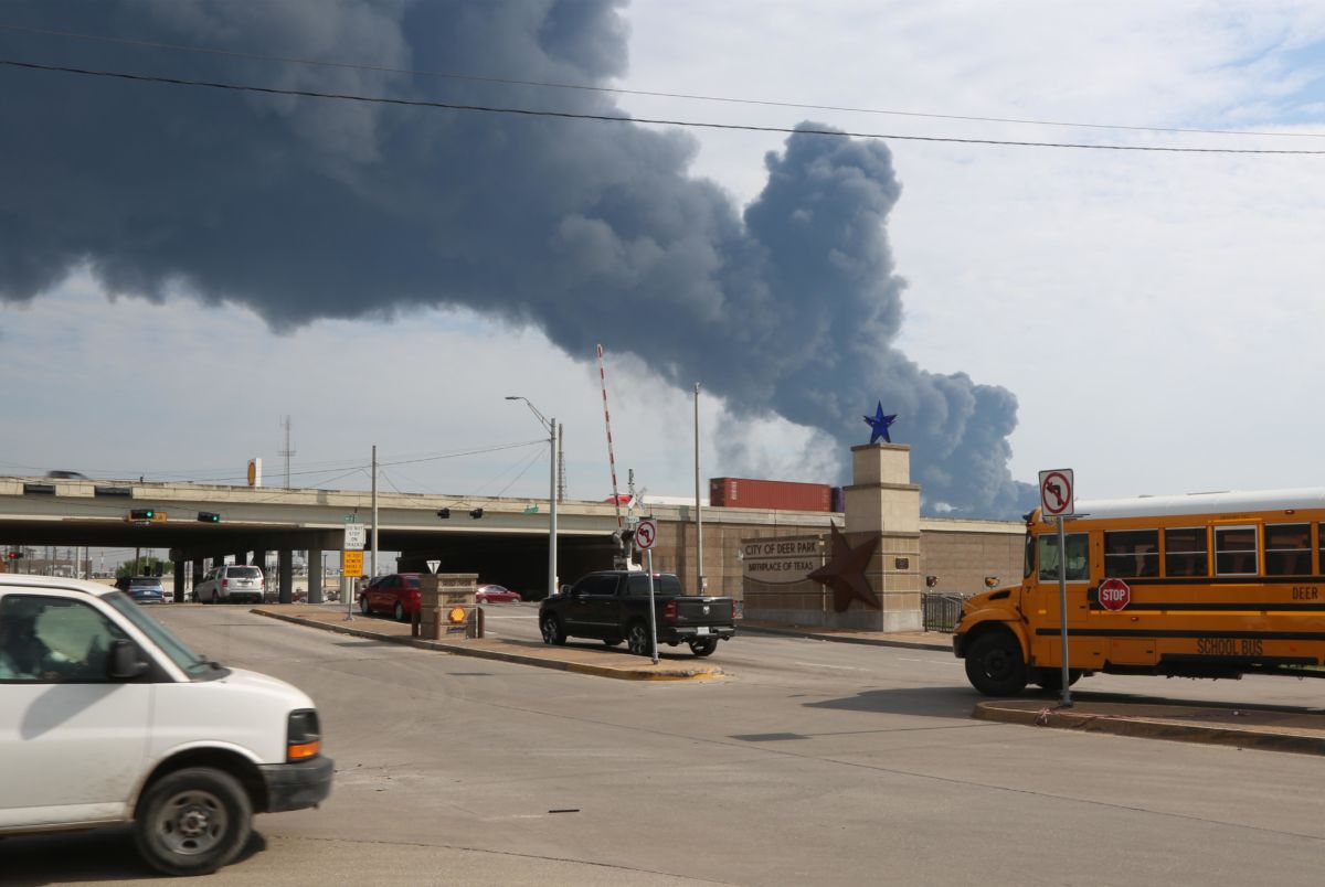 Smoke rises on the horizon as cars and a school bus drive on the highway