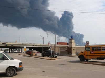 Smoke rises on the horizon as cars and a school bus drive on the highway