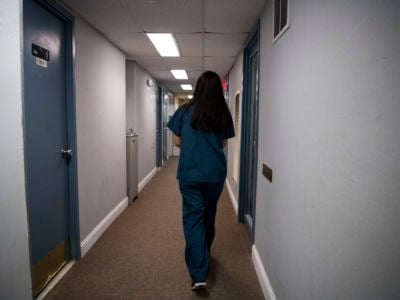 A woman in teal scrubs walks down a clinic hallway