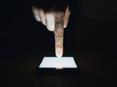 A closeup of a white hand touching a lit smartphone screen