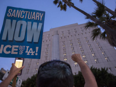 A protester holds a blue sign in front of a tall prison building