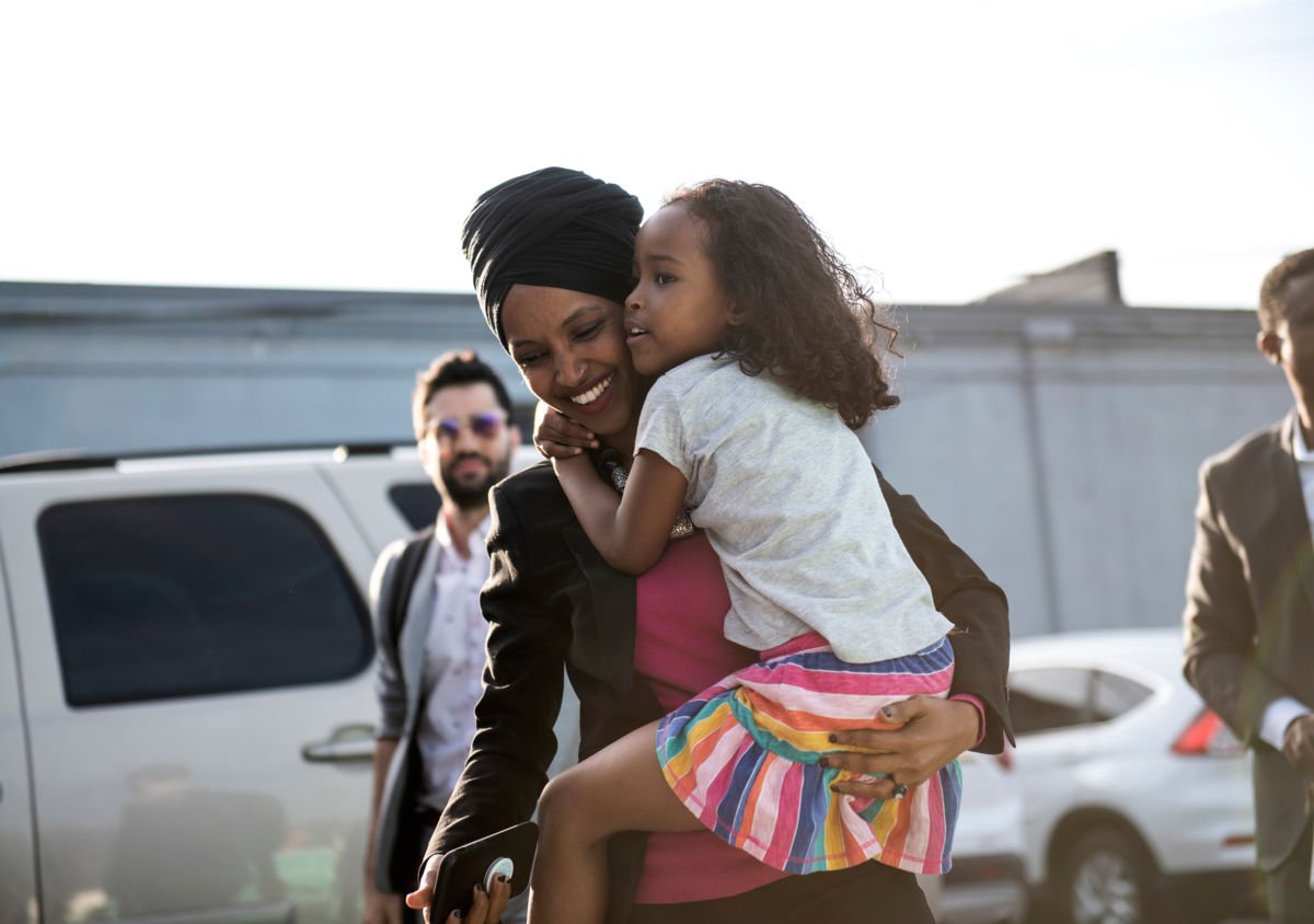 Ilhan Omar smiles while carrying her daughter