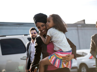 Ilhan Omar smiles while carrying her daughter