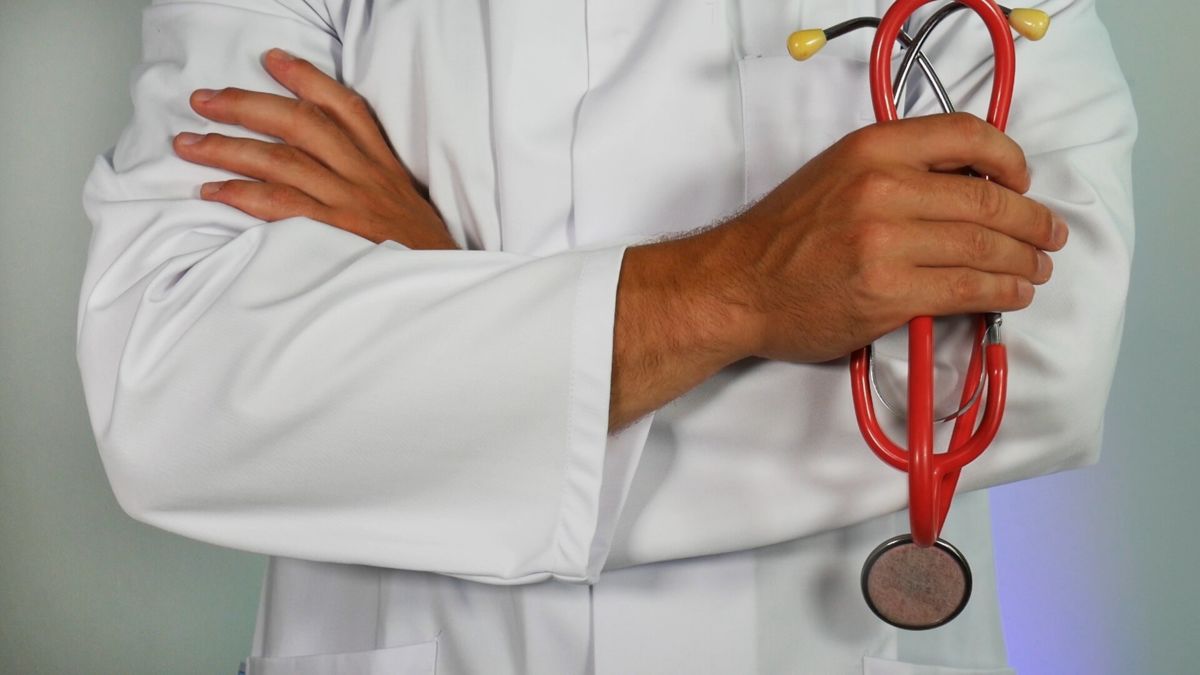 A doctor stands with arms crossed as he holds a red stethoscope.