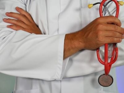 A doctor stands with arms crossed as he holds a red stethoscope.