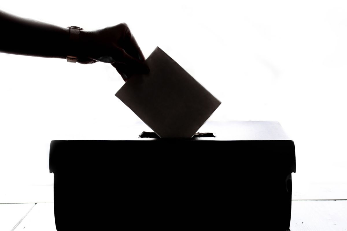 A shadowy hand places a ballot in a box.