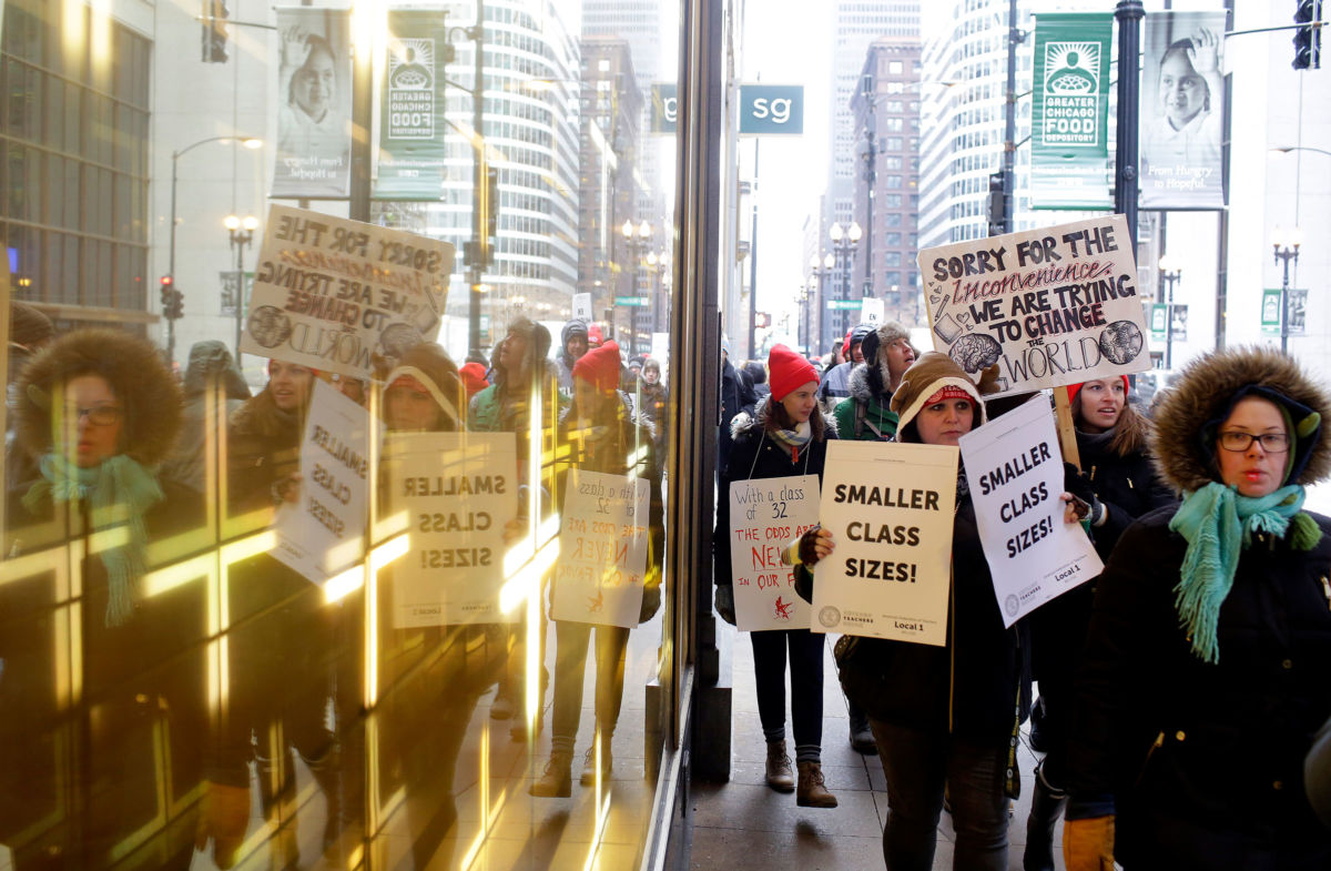 Educators from the Acero charter school network are reflected in a window as they hold signs during a strike outside Chicago Public Schools headquarters on December 5, 2018, in Chicago, Illinois. Chicago charter school teachers were the first of their kind to go on strike in U.S. history.