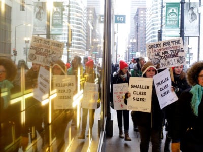 Educators from the Acero charter school network are reflected in a window as they hold signs during a strike outside Chicago Public Schools headquarters on December 5, 2018, in Chicago, Illinois. Chicago charter school teachers were the first of their kind to go on strike in U.S. history.
