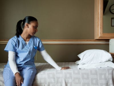 A nurse sits on an empty bed and looks sadly at the pillow