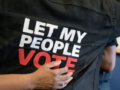 Someone wears a vest reading "LET MY PEOPLE VOTE"