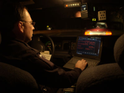 A police officer views a laptop screen while in his cruiser