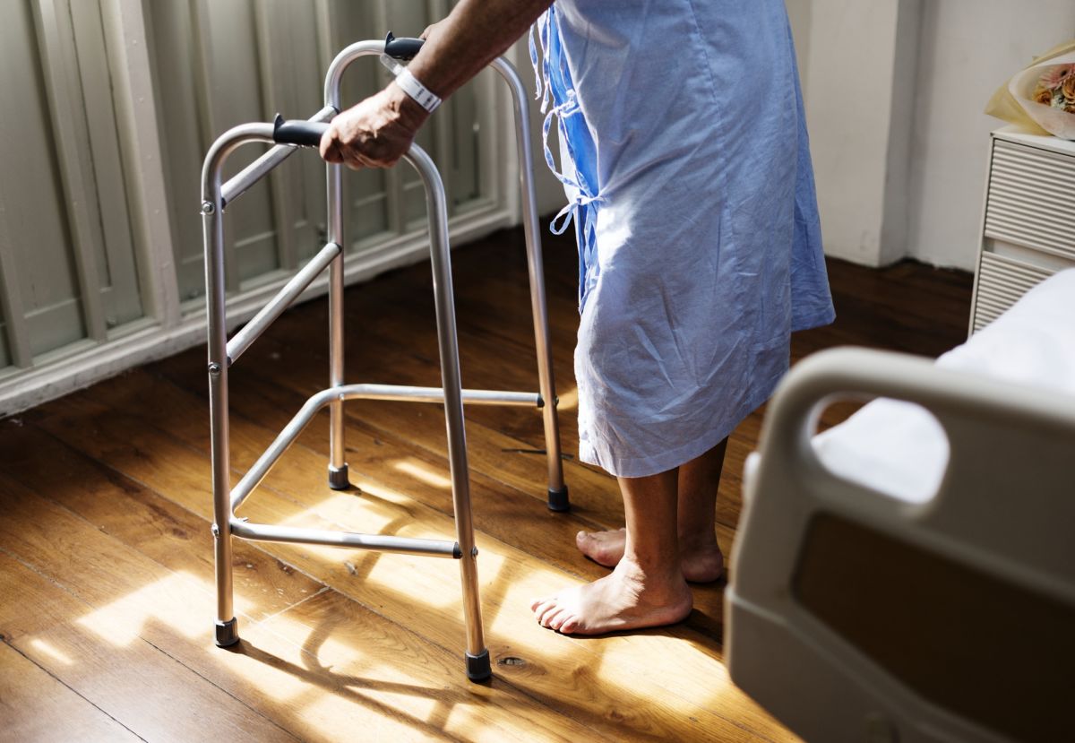 An elderly person getting out of a hospital bed and standing with a walker