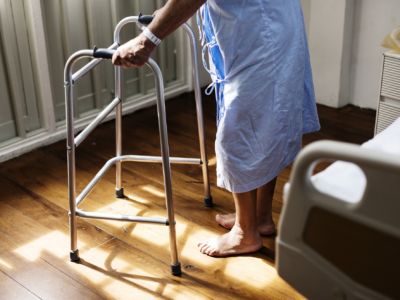 An elderly person getting out of a hospital bed and standing with a walker