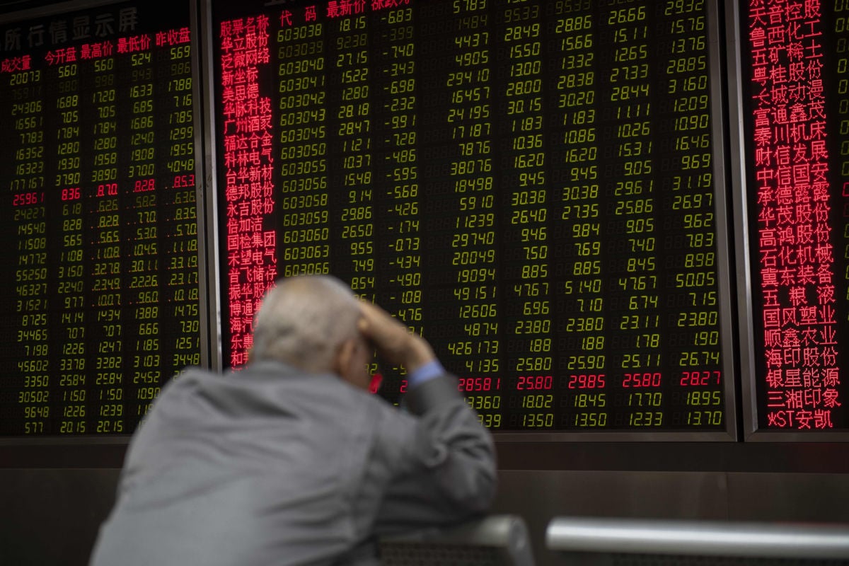 A man holds his head while watching stock prices on a lit screen