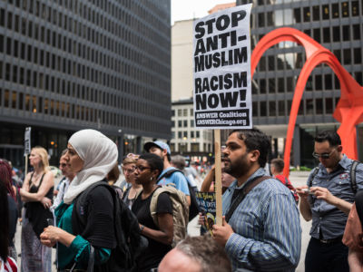 Muslim protesters display signs in front of a large orange statue