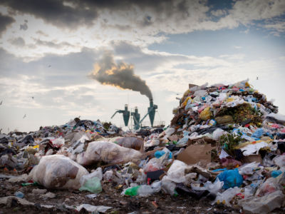 Smokestacks release smog into the air while surrounded by plastic garbage