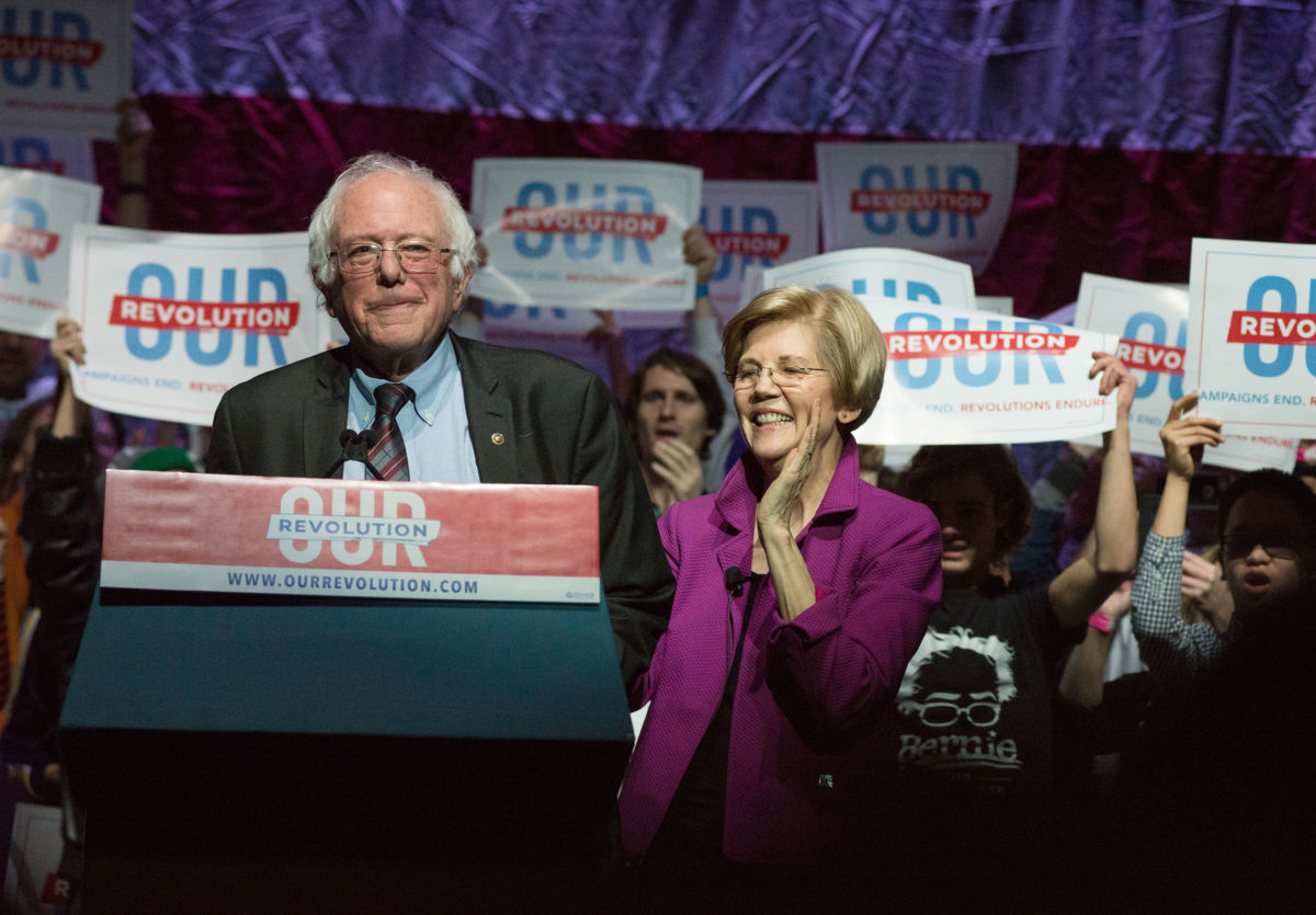 Elizabeth Warren and Bernie Sanders stand at a podium
