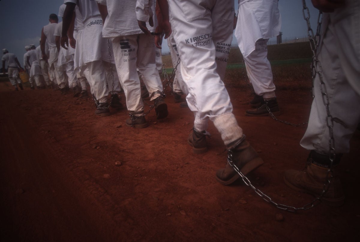 Legs bound by shackles walk through dusty red soil
