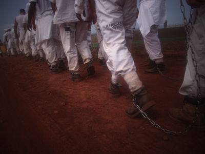 Legs bound by shackles walk through dusty red soil