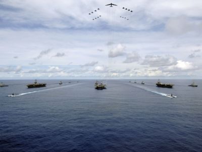 A fleet of naval vessels and associated aircraft are seen in the ocean