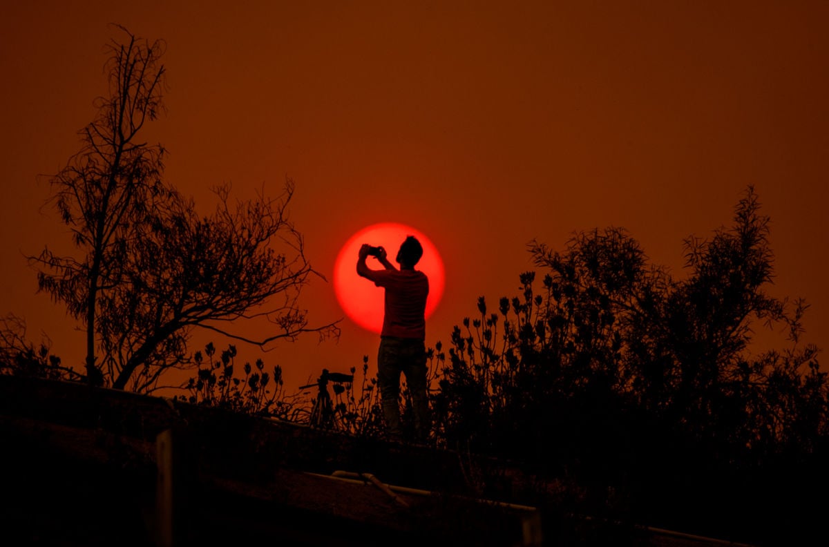 A man is silhouetted against the sun in a smoke-filled sky