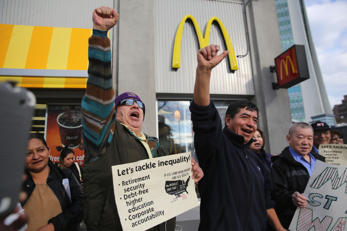 Protesters raise their fists and chant while holding signs outside a McDonalds