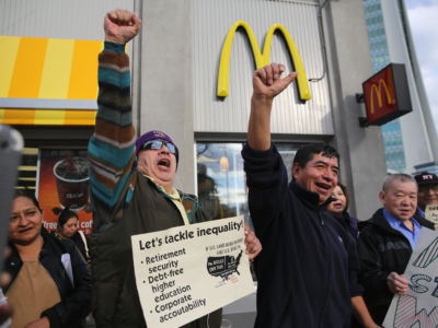 Protesters raise their fists and chant while holding signs outside a McDonalds