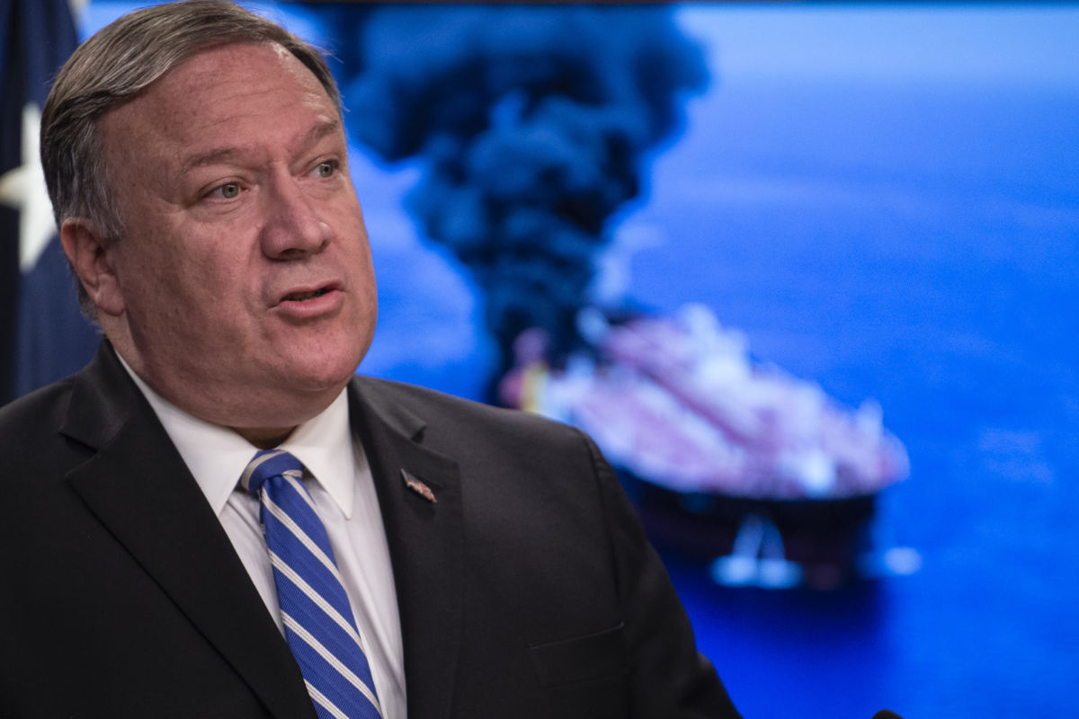 Mike Pompeo stands in front of a photo of a burning tanker, oil